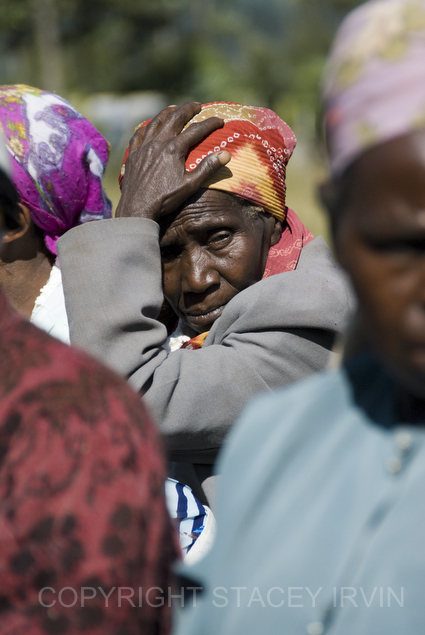 A grandmother waits in the bright sun for the meeting to begin.