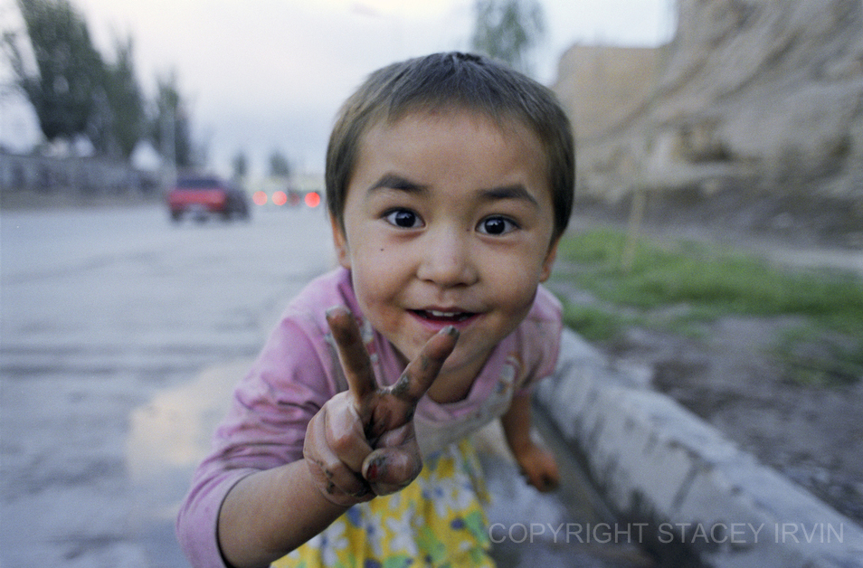 Interrupted while playing in a roadside puddle near Kashgar’s Old Town, this Uighur girl shows a spontaneous and enthusiastic sign for peace.