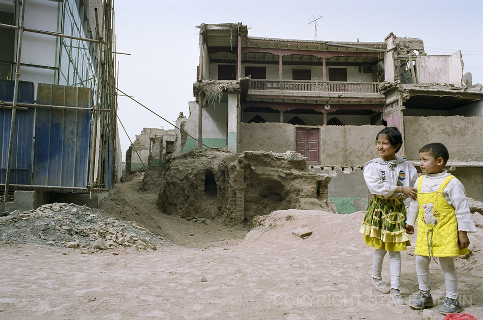 Two Uighur girls stand in front homes that are being demolished (right) to make way for new commercial shopping areas (left) in a residential area near Id Kah Mosque in Kashgar.